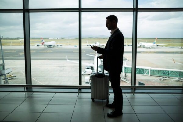 Businessman with luggage using mobile phone at airport