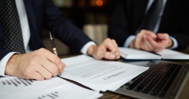 Closeup portrait of unrecognizable successful businessman wearing black formal suit reviewing documents and signing contract during meeting